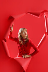 Young woman visible through hole in red paper