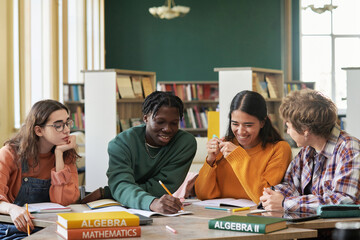 Group of high school students sitting at a table in bright library, engaging in a study session. Various textbooks on math subjects spread across table