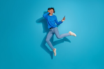 Obraz premium Full body photo of attractive young man jump excited dance headphones dressed stylish clothes isolated on blue color background