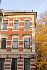 Obraz premium facade of historic building is tree with autumn yellow leaves. brick house of historical architecture in autumn season. urban landscape. tourist destinations, famous place in business part metropolis.