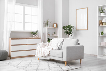 Interior of light living room with grey sofa, shelf units and commode