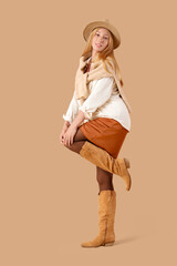 Beautiful young woman in hat with sweater on brown background