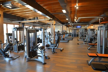 A spacious fitness center featuring various strength training and cardio machines, illuminated by natural light streaming through large windows.