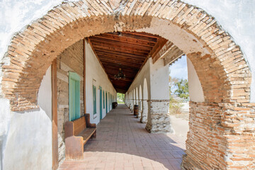 View through stone archway of a long collonade in front of a long Spanish-style stone and wood...