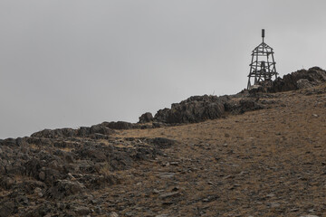 Landscape of the hilly rocky steppe in fade autumn colors in Mongolia. A place similar to the lands of the Orcs. On the peak of a hill is a wooden military signal construction like a cell.