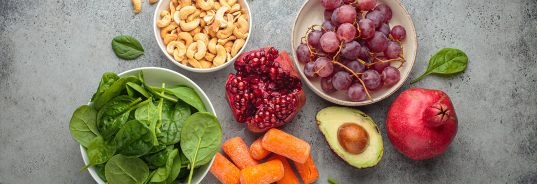 Assortment of healthy potassium rich foods including cashews, grapes, avocado, pomegranate, baby carrot and spinach placed on a gray background, a balanced diet for wellness