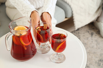 Beautiful young woman with glasses of delicious mulled wine sitting on sofa at home, closeup
