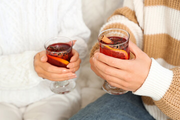 Couple with glasses of delicious mulled wine sitting on sofa at home, closeup