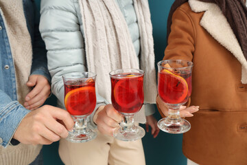 Friends with glasses of delicious mulled wine on blue background, closeup