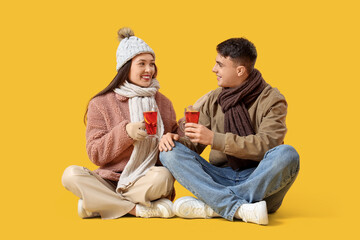 Happy couple with glasses of delicious mulled wine sitting on yellow background