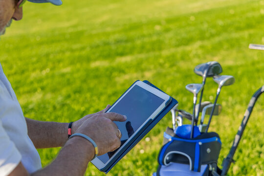 Close-up of senior golfer using tablet on golf course next to golf bag