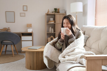 Young woman with warm plaid and cup of coffee at home on winter day