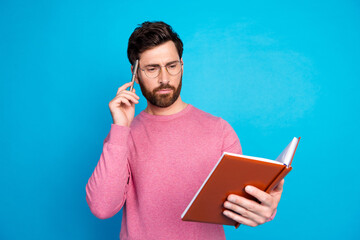 Thoughtful man in glasses holding a notebook and pen, contemplating ideas against a blue background