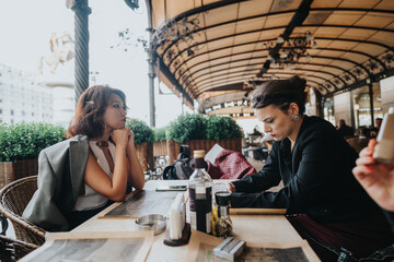 Two businesswomen engaged in a focused meeting at an outdoor cafe. The relaxed atmosphere combines with a professional setting, showcasing teamwork and collaboration in a casual yet effective