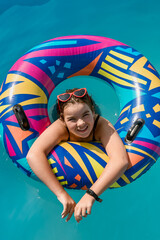 cute happy girl 12 years old swims in a pool with blue water in a bright circle. High quality photo