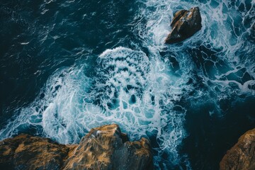 Powerful waves collide with rocky formations at the coastline, creating a stunning display of white foam against the vibrant blue water during the evening light.