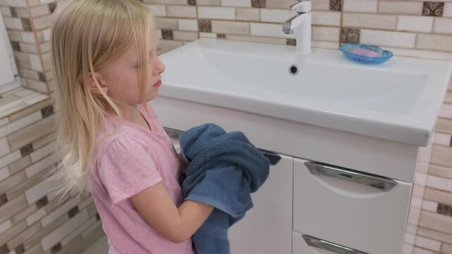 Young girl drying her hands with a blue towel while standing in front of a bathroom sink after washing