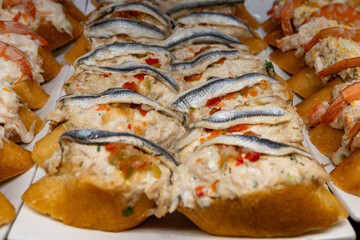 Typical snacks of Basque Country, variety of pinchos or pinxtos oven baked sea food, bread, anchovy, shrimps salad, cheese served in bar in San-Sebastian or Bilbao, Spain