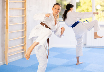 Two female karateka focused intently on perfecting their roundhouse kicks during training.