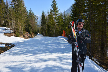A skier stands on a ski slope in the perspective in the forest between the trees and smiles