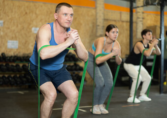 Focused sporty adult man taking part in intense group training in gym exercising with resistance...