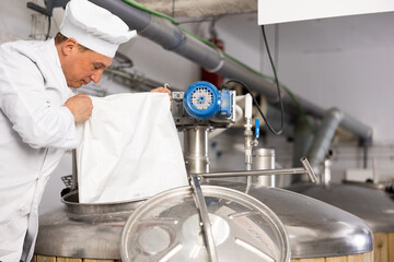 Man brewer in white coat pouring beer yeast into tank in beer factory.