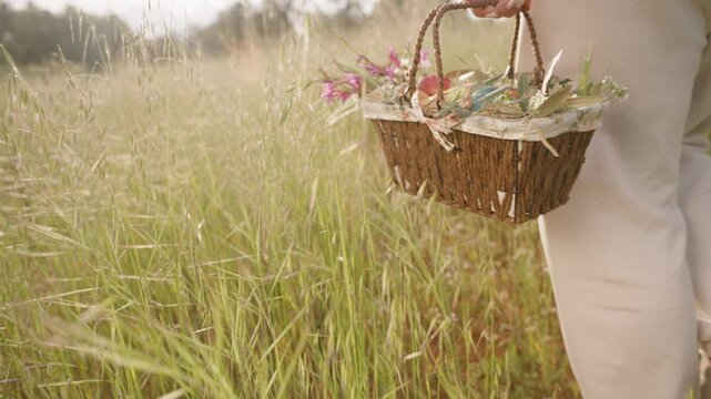 A Close-Up of a Basket Filled with Colorful Easter Eggs and Flowers, as a Woman Walks Through a Grassy Field. Slow motion.