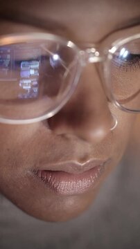 Vertical. Close up of reflection of computer screen on the glasses of an African American hacker woman working on her laptop in the dark. Young people and security of computer networks and Internet. 