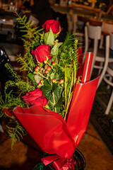 A bouquet of red roses in red paper in a restaurant at night