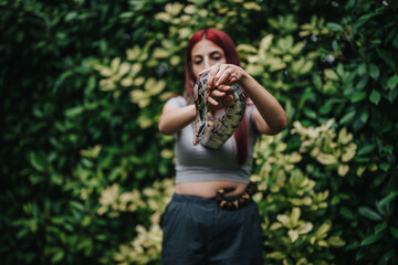 A girl confidently holds a snake in a vibrant garden, showcasing an intimate connection with nature and wildlife. The lush greenery enhances the tranquil and adventurous atmosphere.