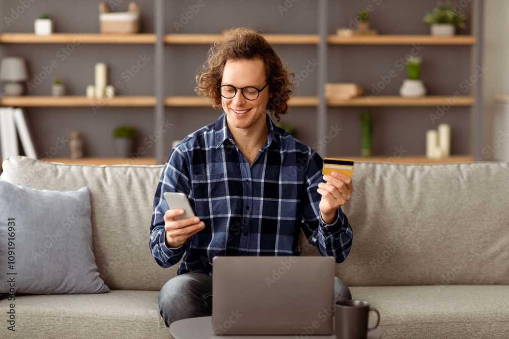 Poster happy guy using credit card and smartphone shopping online in mobile application sitting at laptop o