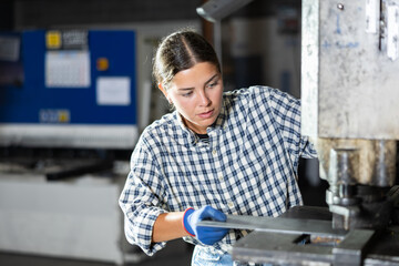 Focused young female worker operating hydraulic punch press in manufacturing facility, creating...