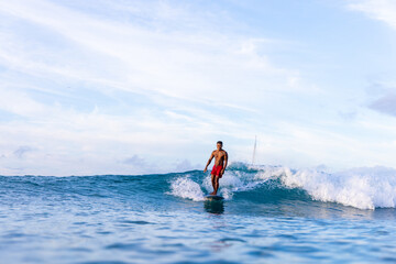 A man in red shorts is surfing on a wave in the ocean. The sky is blue