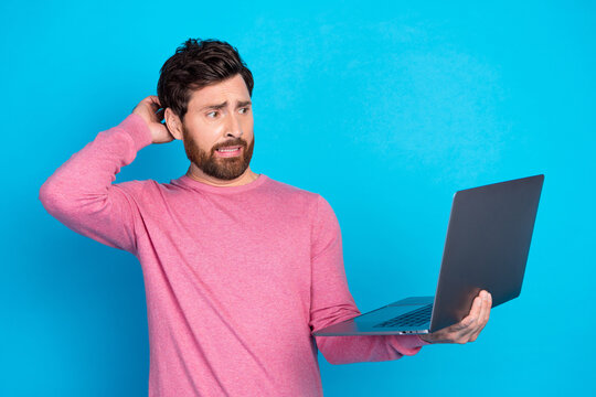 Confused man with laptop in pink sweater isolated on blue background pondering technology or online issues