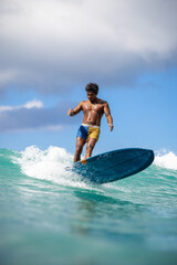 A man is surfing on a blue surfboard in the ocean. The sky is cloudy, but the water is clear