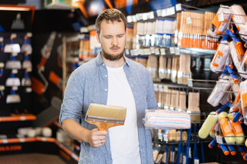 Man chooses paint roller and paint brush at a local hardware store