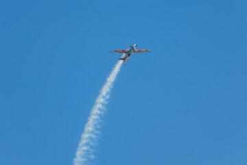 Stunt aerobatic plane performing stunts in blue sky with smoke trail. Concept of speed, difficulty, precision, risk, challenge