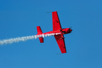 Fototapeta premium Red stunt aerobatic plane performing stunts in blue sky. Concept of speed, difficulty, precision, risk