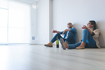 A man and woman are sitting on the floor in a new home, drinking wine. New home concept.