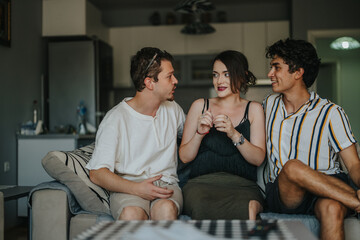 Naklejka premium A group of three young adults engaging in lively conversation on a sofa in a warm, inviting living room atmosphere.