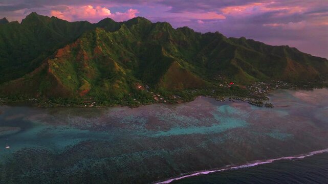 Deep purple pink sunset bungalows Moorea island Cooks Opunohu bay French Polynesia aerial drone blue lagoon coral reef Mount Mauaroa Tohivea Rotui jagged peaks Haapiti Paopao Pacific Ocean forward