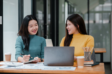 Obraz premium Two Young Women Collaborating in Modern Office Setting with Laptop and Coffee