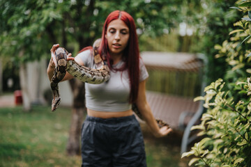 A young girl with red hair carefully handles a snake outdoors. The garden setting is vibrant and...