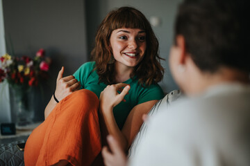A young woman with a bright smile engages in a lively conversation with a friend in a cozy home...