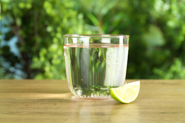 Glass of soda water with lime on wooden table against blurred background