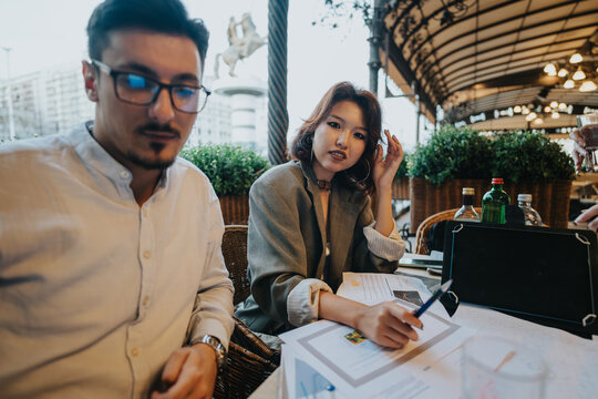 A diverse group of business people engage in a collaborative meeting at a coffee bar. They are discussing project ideas and analyzing documents in a relaxed outdoor setting.