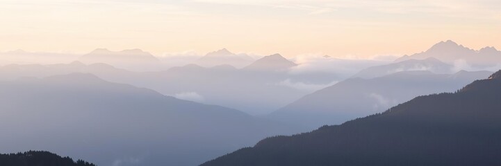 Naklejka premium Mountain landscape with alpine peaks through morning fog, dawn scenery, early morning light, snow-capped peaks