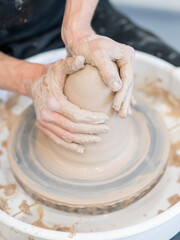 Close-up of a potter's hands working on a pottery wheel. Vertical photo. 