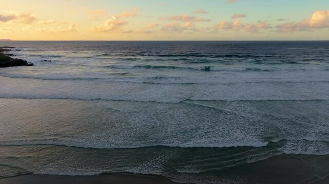 Drone footage of the Atlantic Ocean waves on the sandy shore of Caion at sunset in A Coruna, Spain