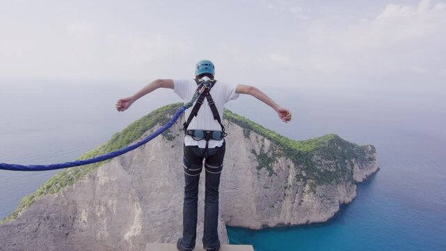 Bungee jumper leaping off Greece cliff over beautiful beach - steady cam shot